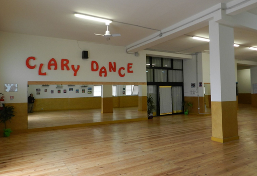 Interno di uno studio di danza con un grande specchio, pavimento in legno e la scritta 