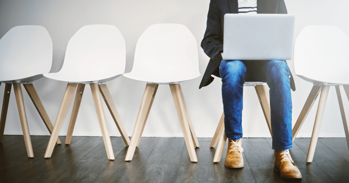 A lone person sitting on a chair with their laptop. The chairs to their left and right are empty