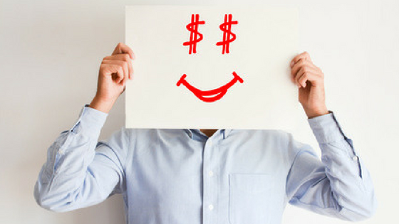 Man in blue shirt holding piece of paper over his face. Piece of paper has a red smiley face drawn on it. The eyes are dollar signs.