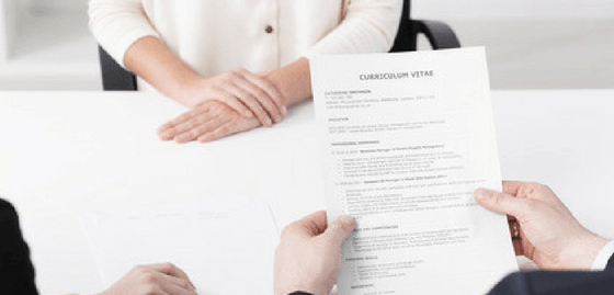 Person sitting across the table from two job interviewers. One job interviewer is hold the person's CV