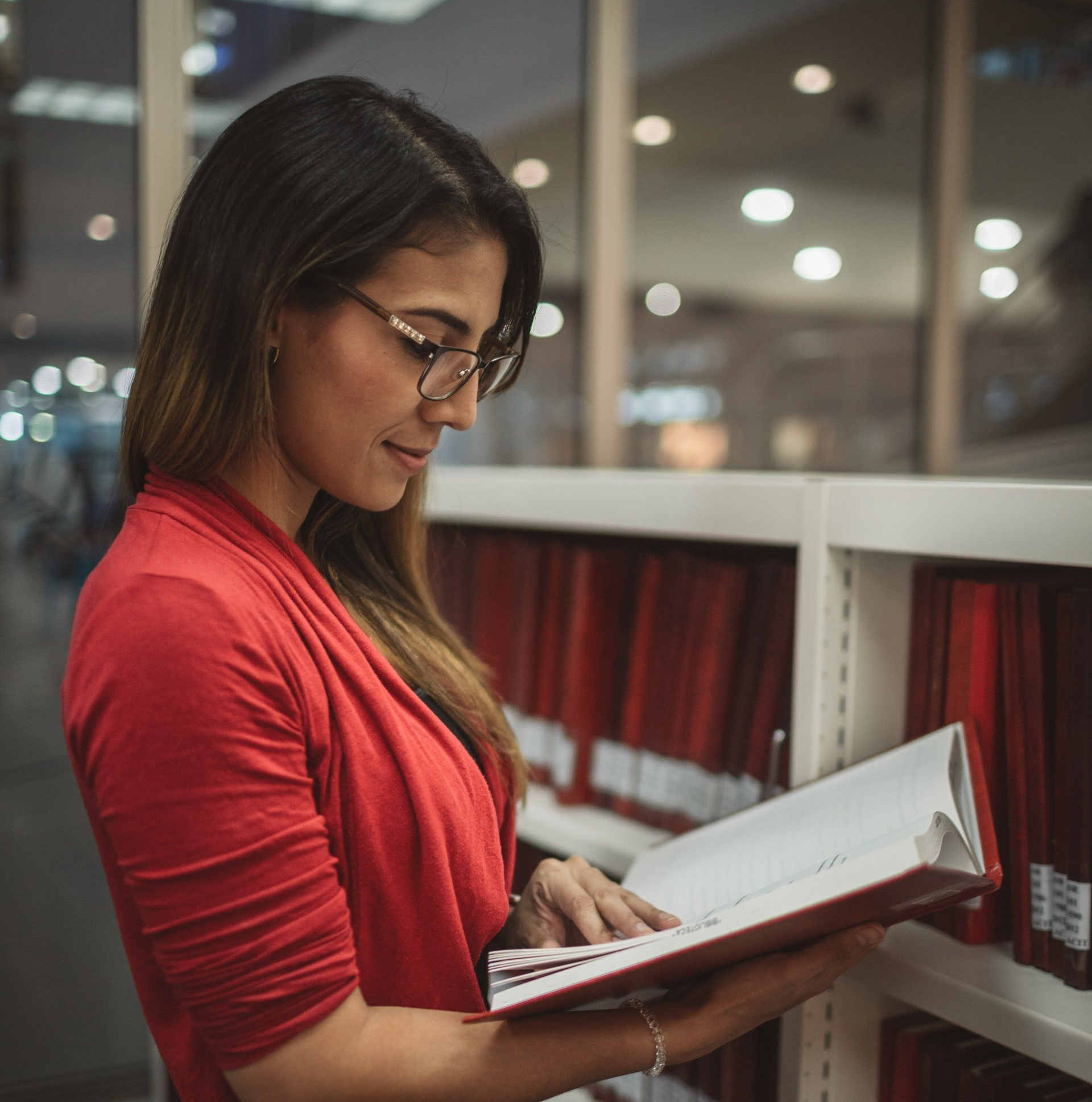Female in a red top wearing glasses scanning a book in a library