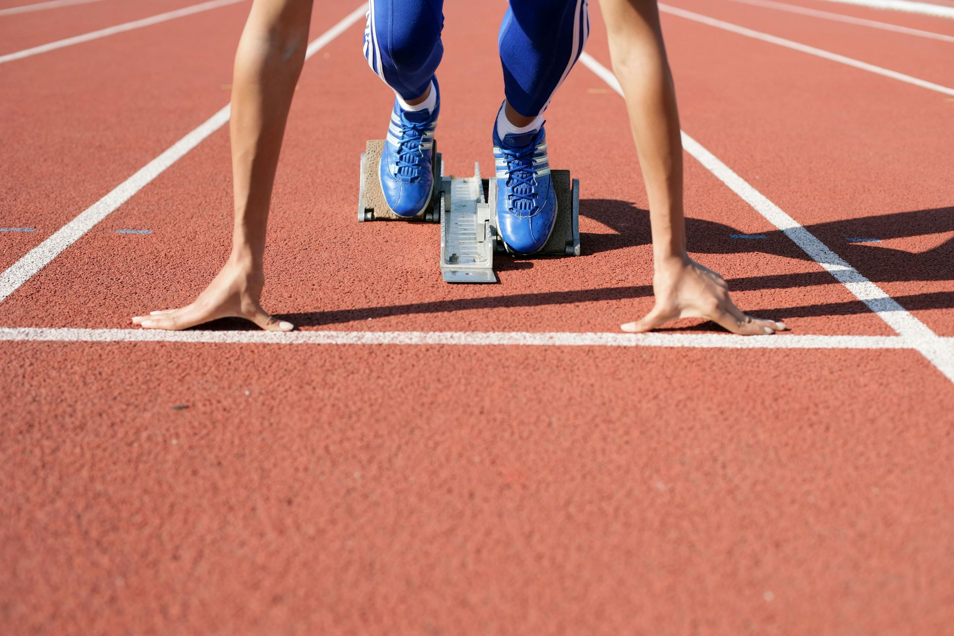 Sprinter in blue shoes crouching at the starting block on a race track