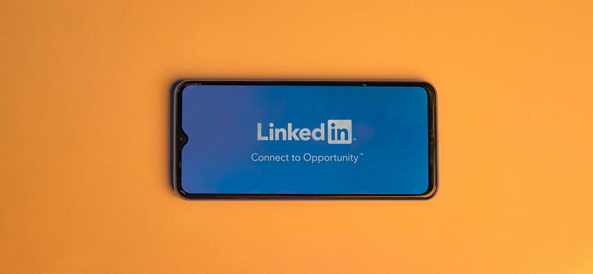 Mobile phone sitting on an orange table. Mobile phone is showing the LinkedIn logo on its screen.