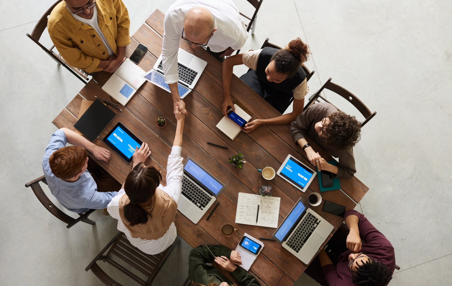 8 employees with their tablets and laptops sitting around a conference table and having a discussion