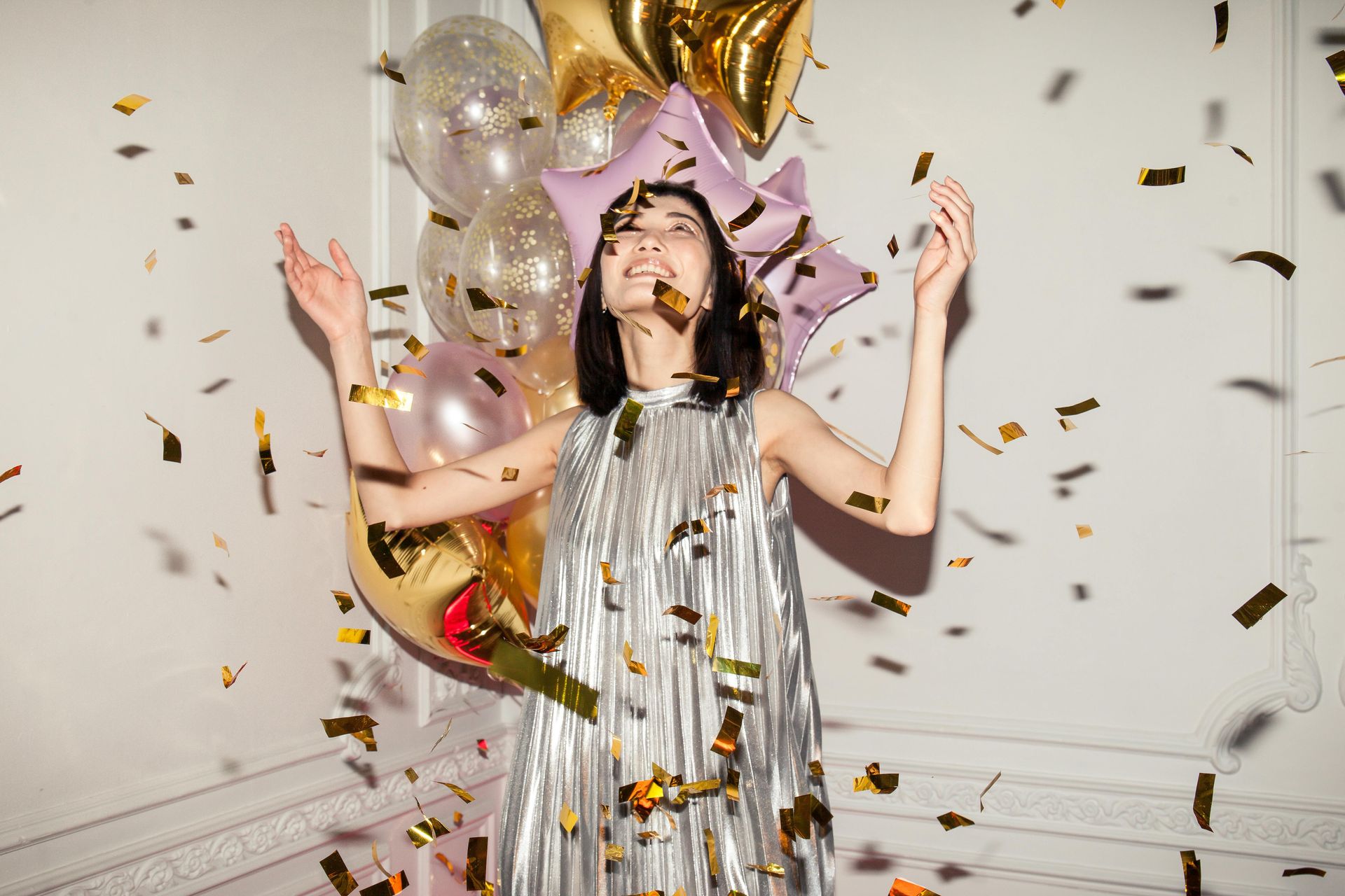 Girl in silver party dress surrounded by confetti and balloons