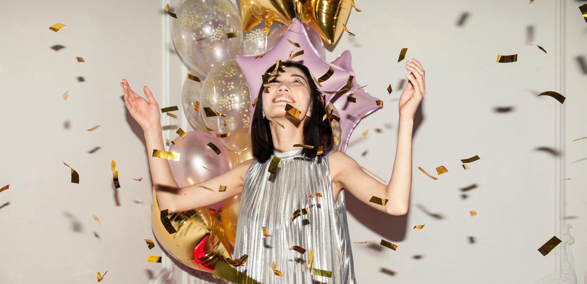 Girl in silver party dress surrounded by confetti and balloons