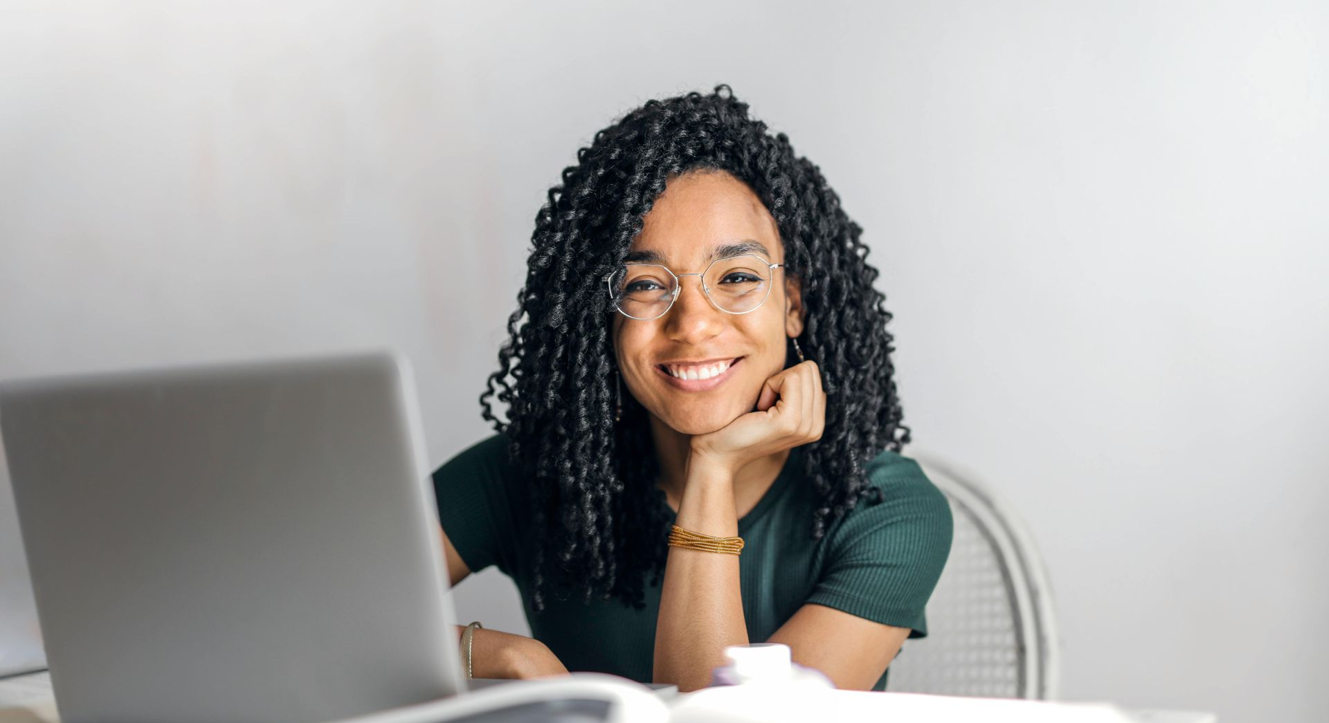 Smiling girl with dark curly hair and glasses sitting in front of a laptop