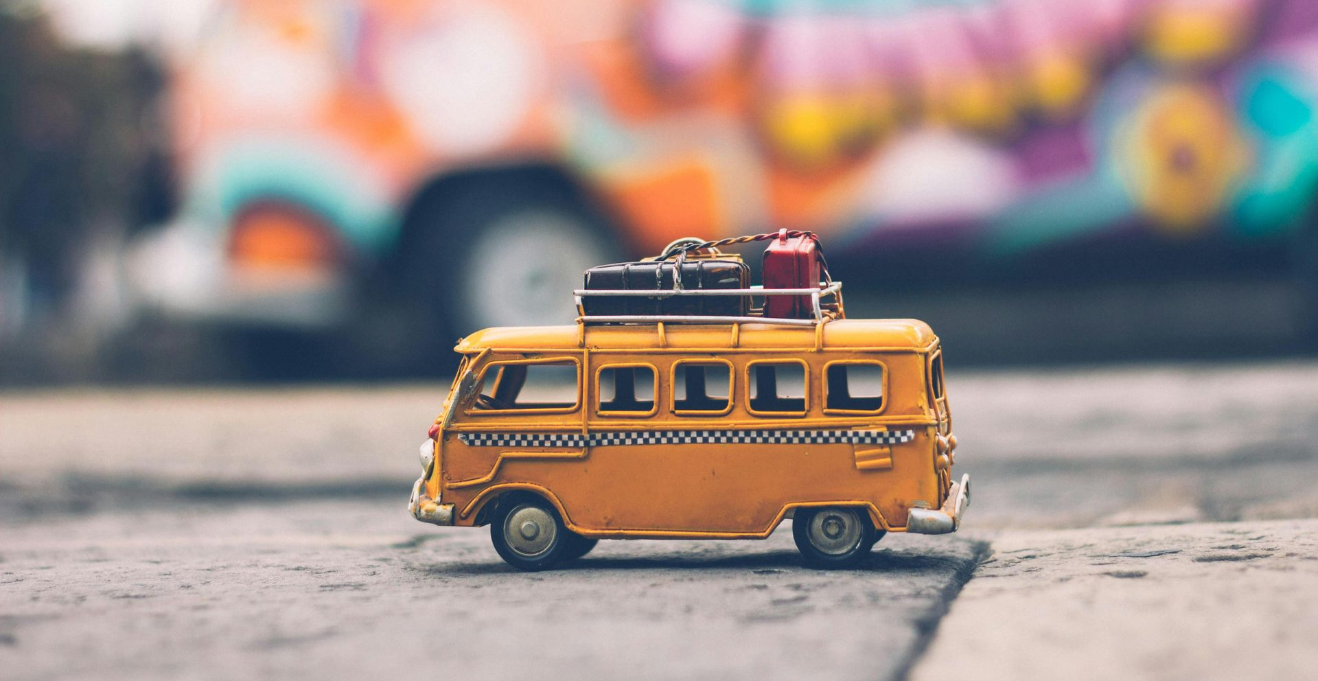 Miniature model of a yellow bus with luggage on top. The bus is on a pavement