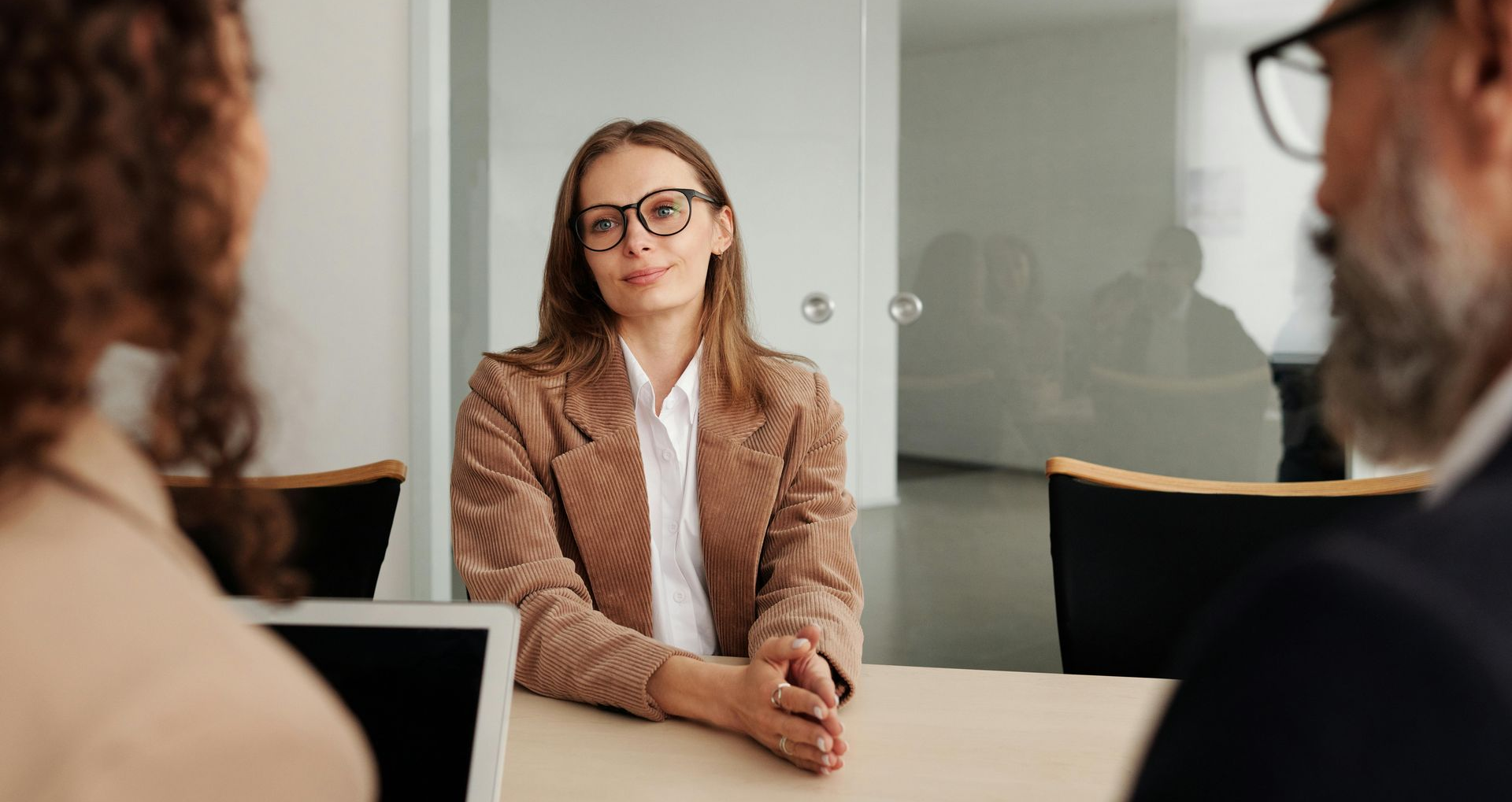 Girl in suit and glasses sitting opposite two people in a meeting room
