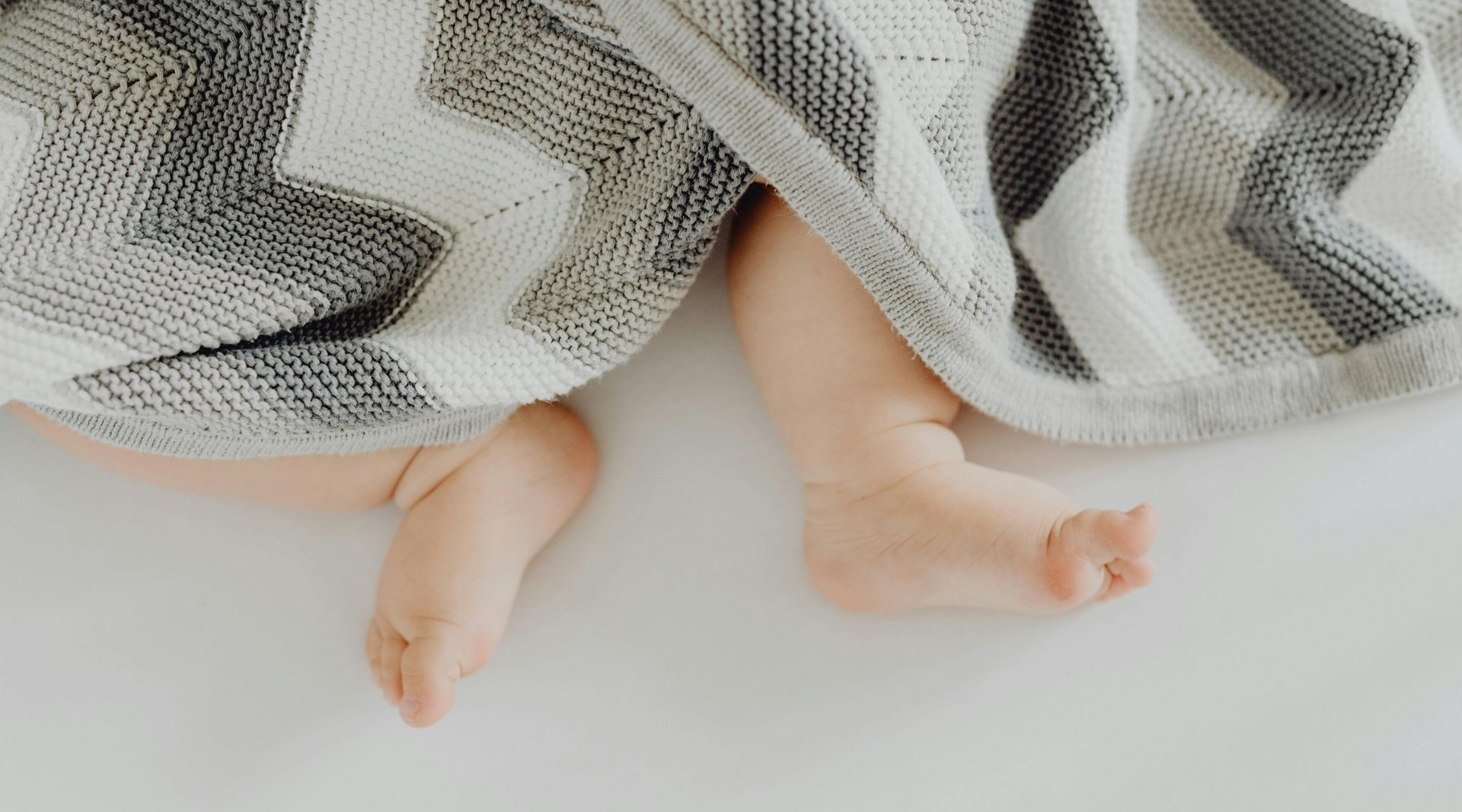 A baby's feet poking out from beneath a baby blanket