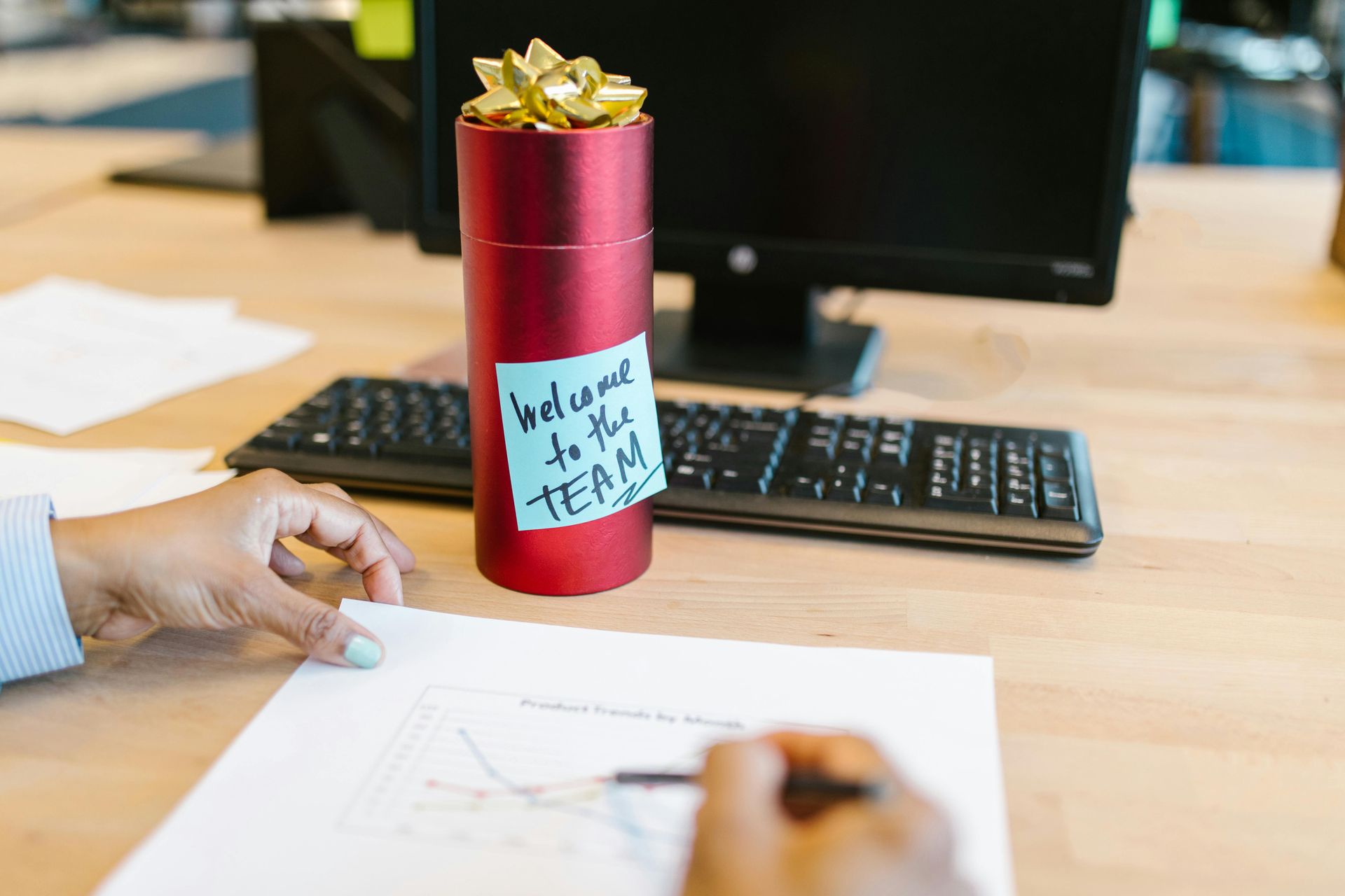 A person at their work desk. There is a gift on the desk with a post-it note saying 'welcome to the team'
