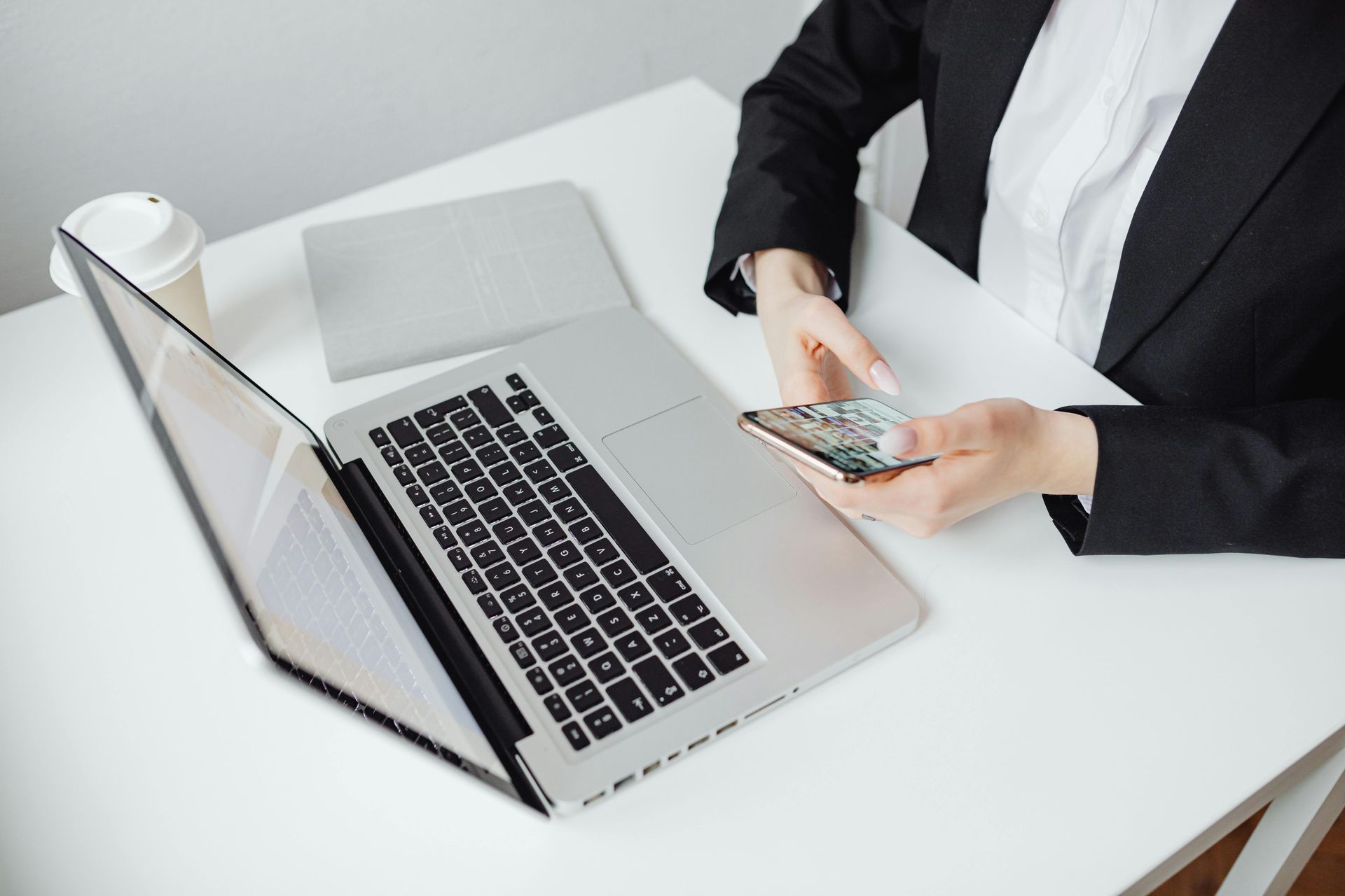 Person sitting in front of a laptop and using their mobile phone