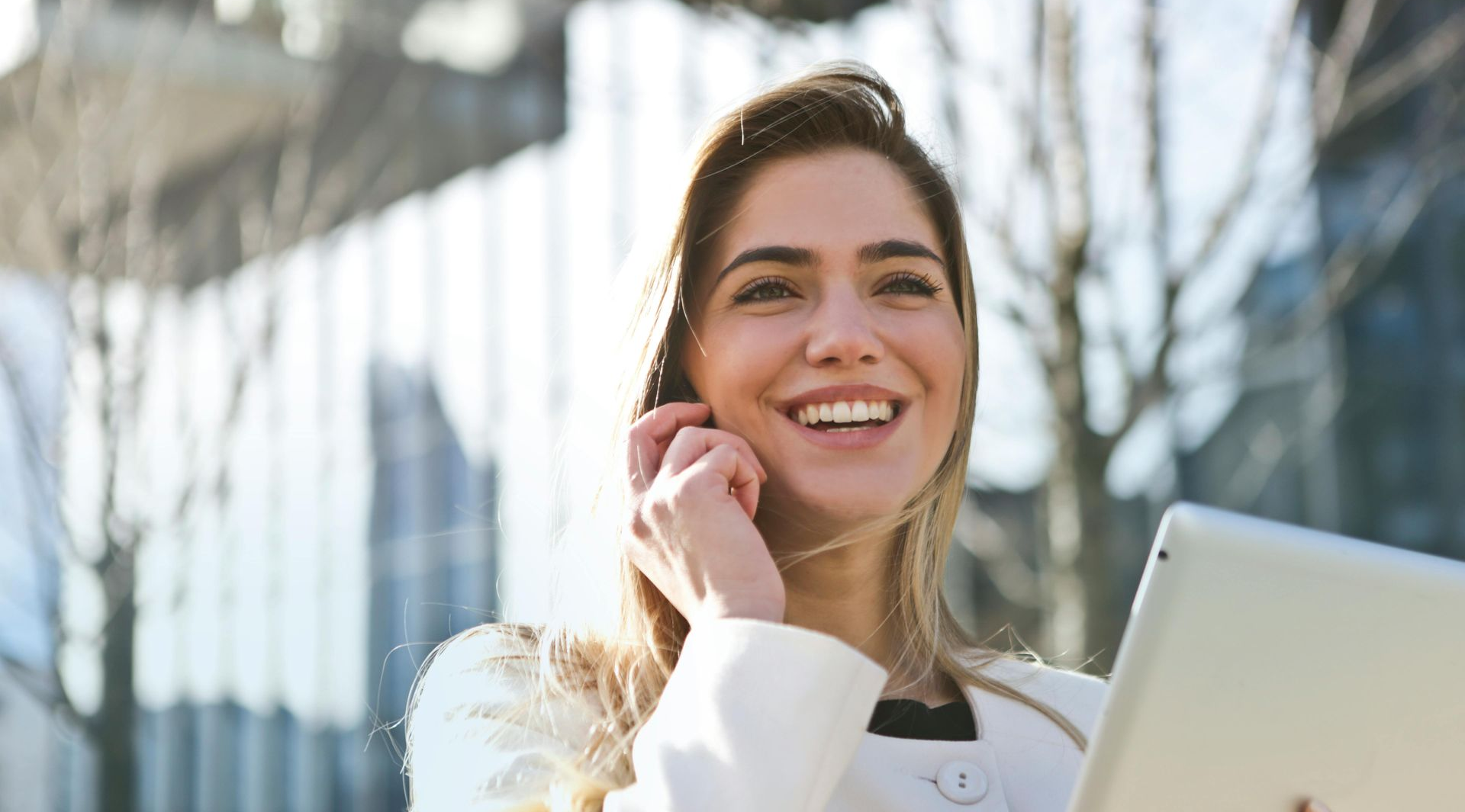 Female  smiling and holding a tablet while standing outside an office building