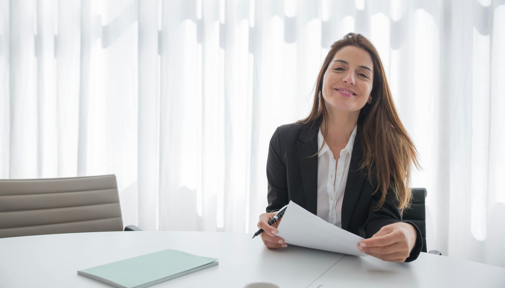 Girl in suit smiling and sitting at a desk holding a piece of paper