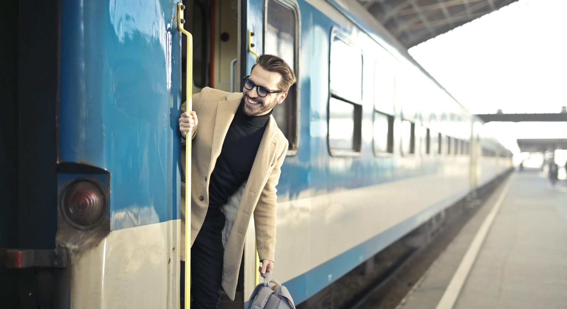 Man in smart attire holding a backpack getting off a train