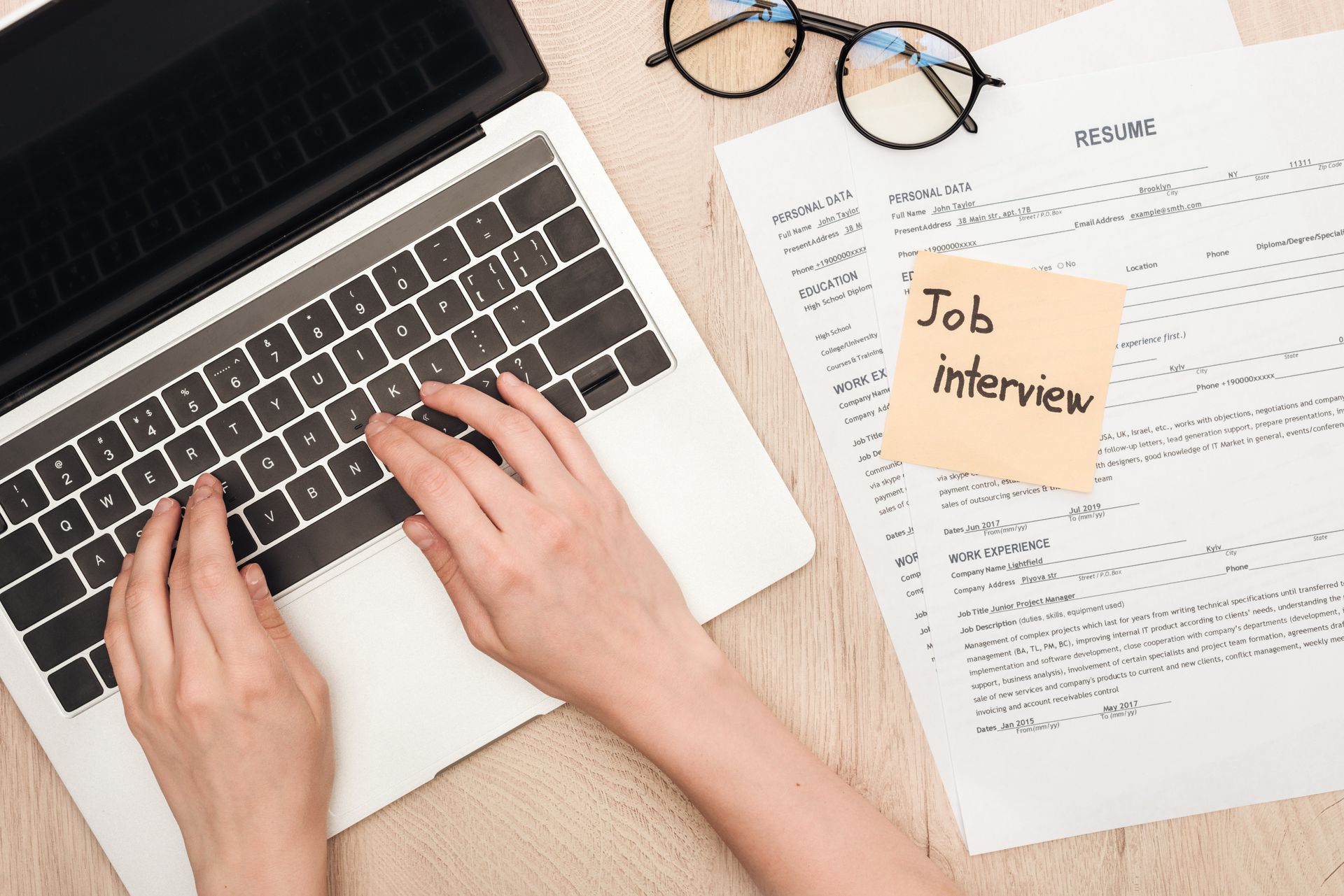 Person typing on their laptop. There are papers next to them with a post-it note saying 'Job Interview'