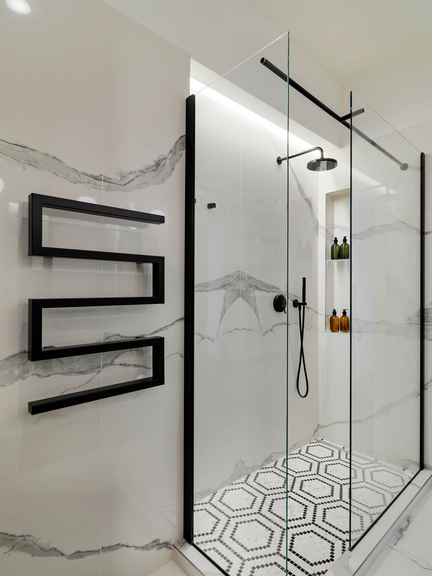 A bathroom with a walk in shower and a black towel rack.