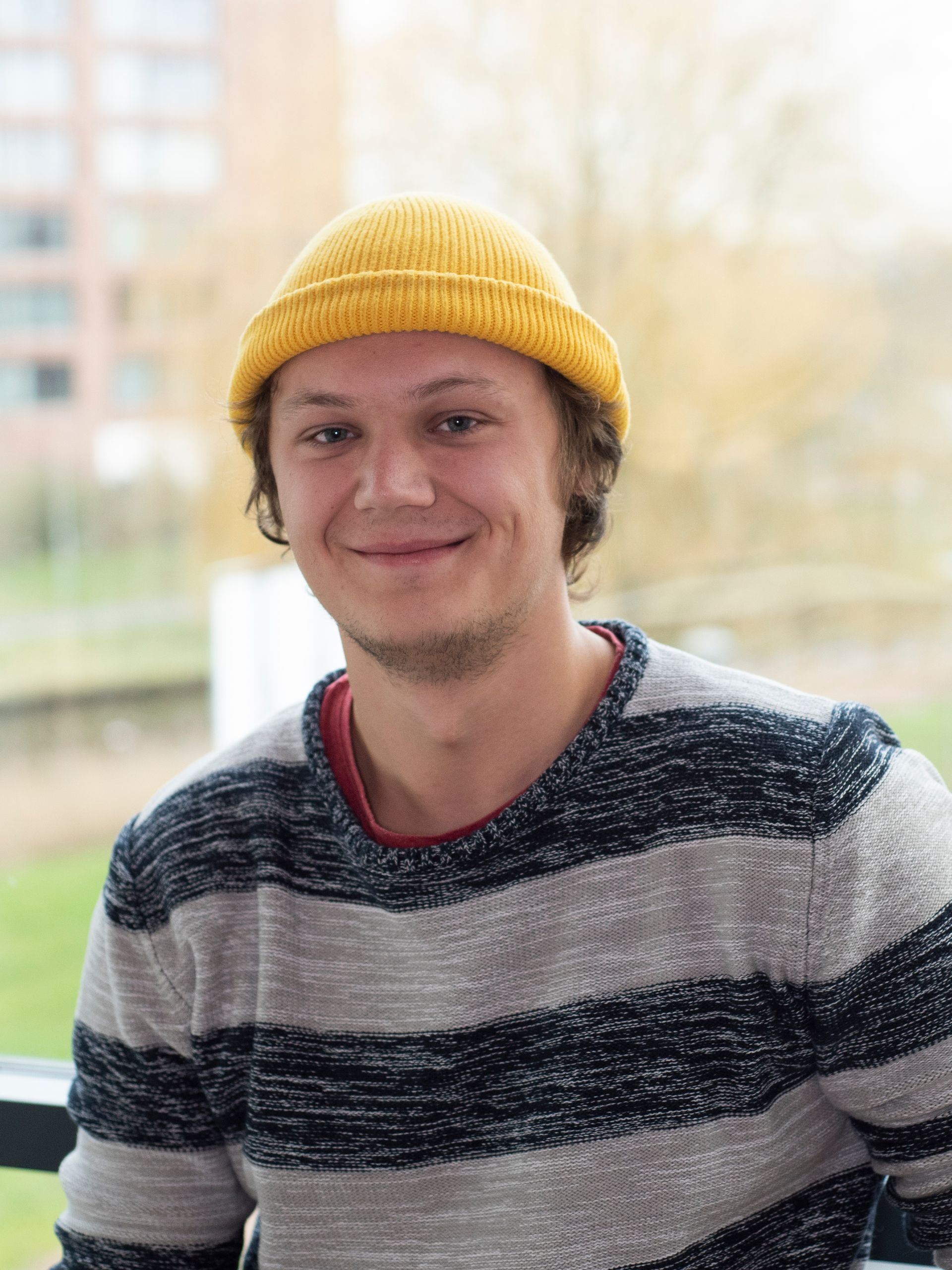 Een jongeman draagt ​​een gele muts en een gestreepte trui en lacht.