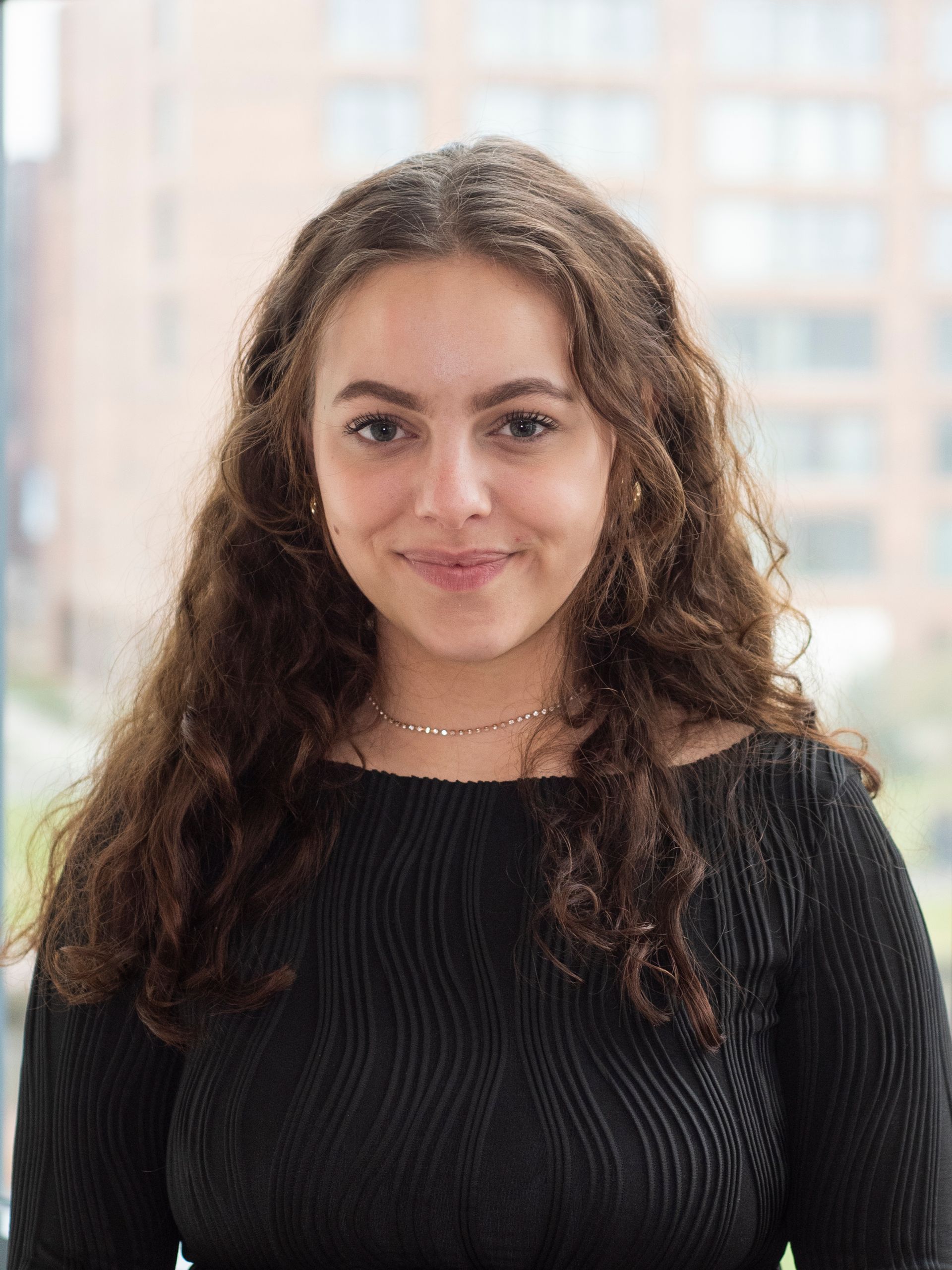 Een jonge vrouw met lang krullend haar draagt ​​een zwarte trui en een ketting.