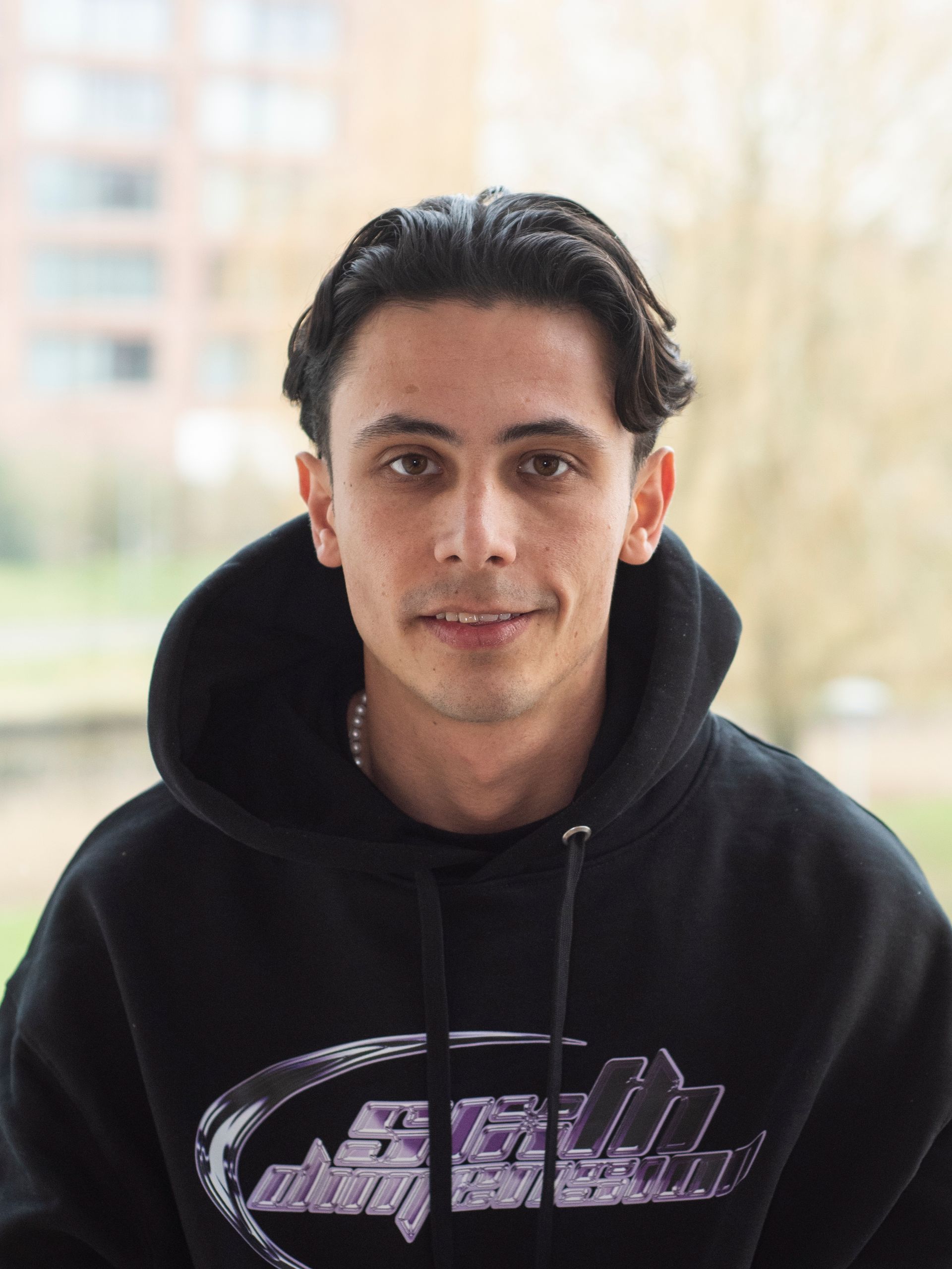 Een jongeman in een zwarte hoodie lacht naar de camera.