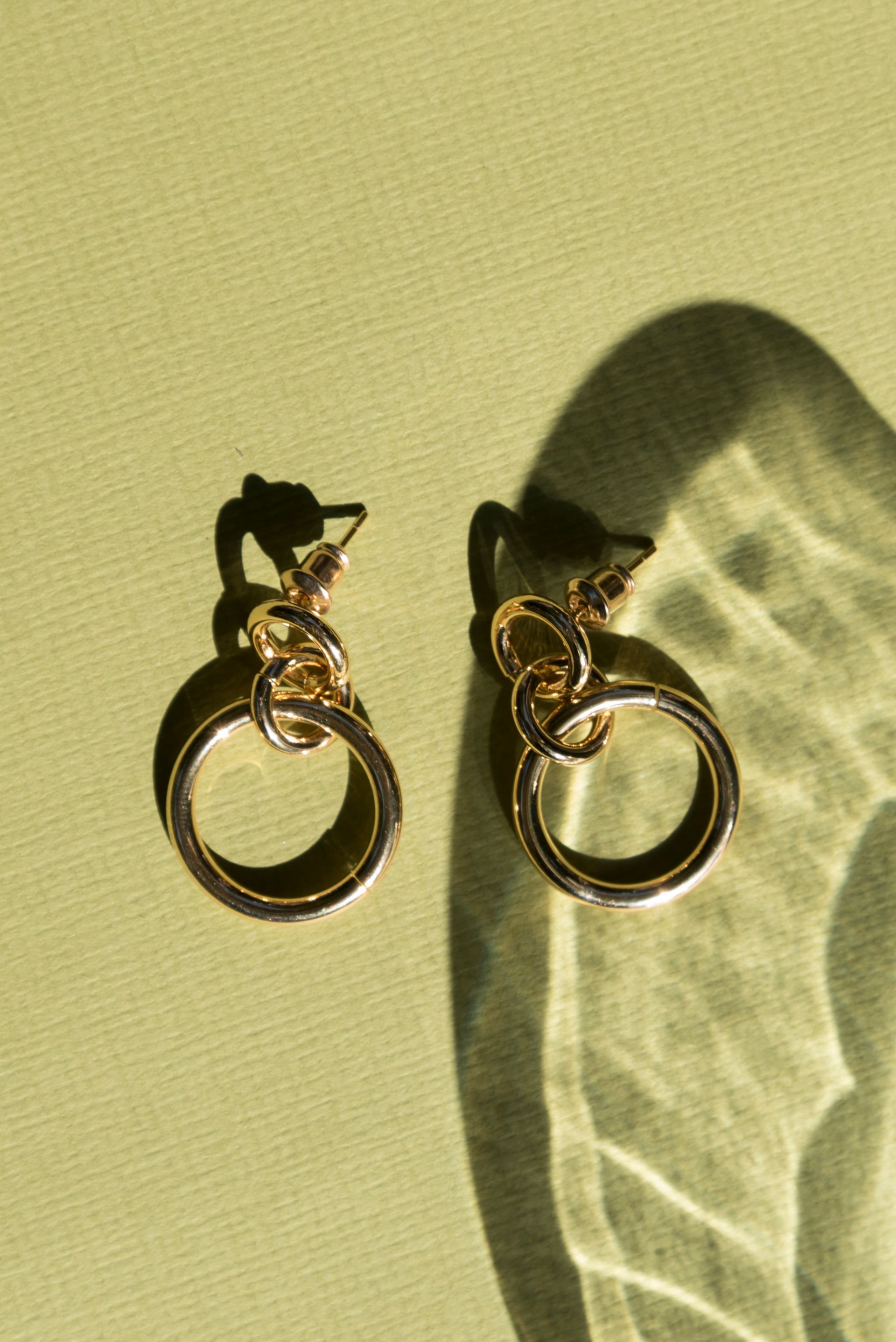 Een paar gouden oorbellen liggen op een groen oppervlak.