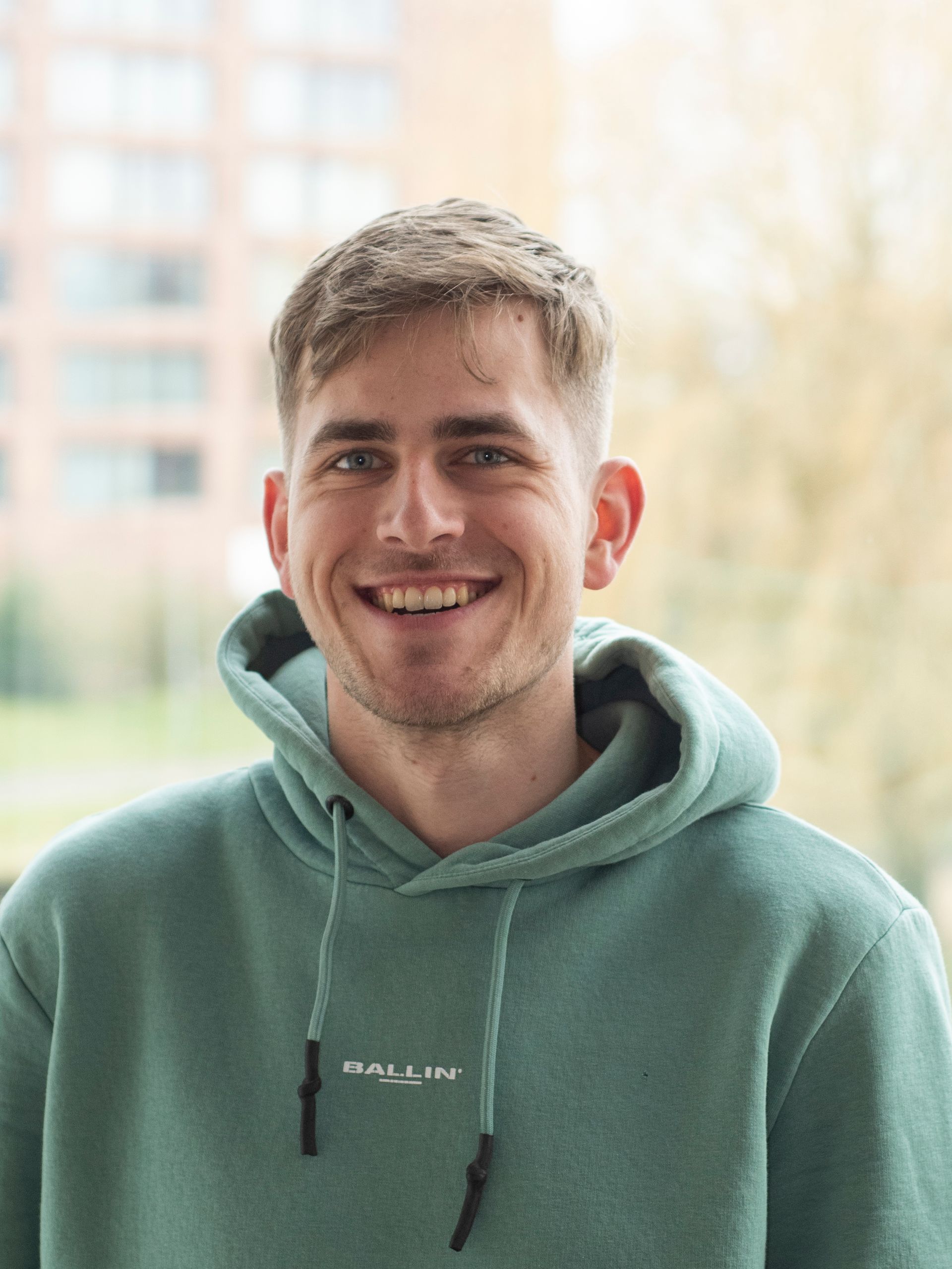Een jongeman in een groene hoodie lacht naar de camera.
