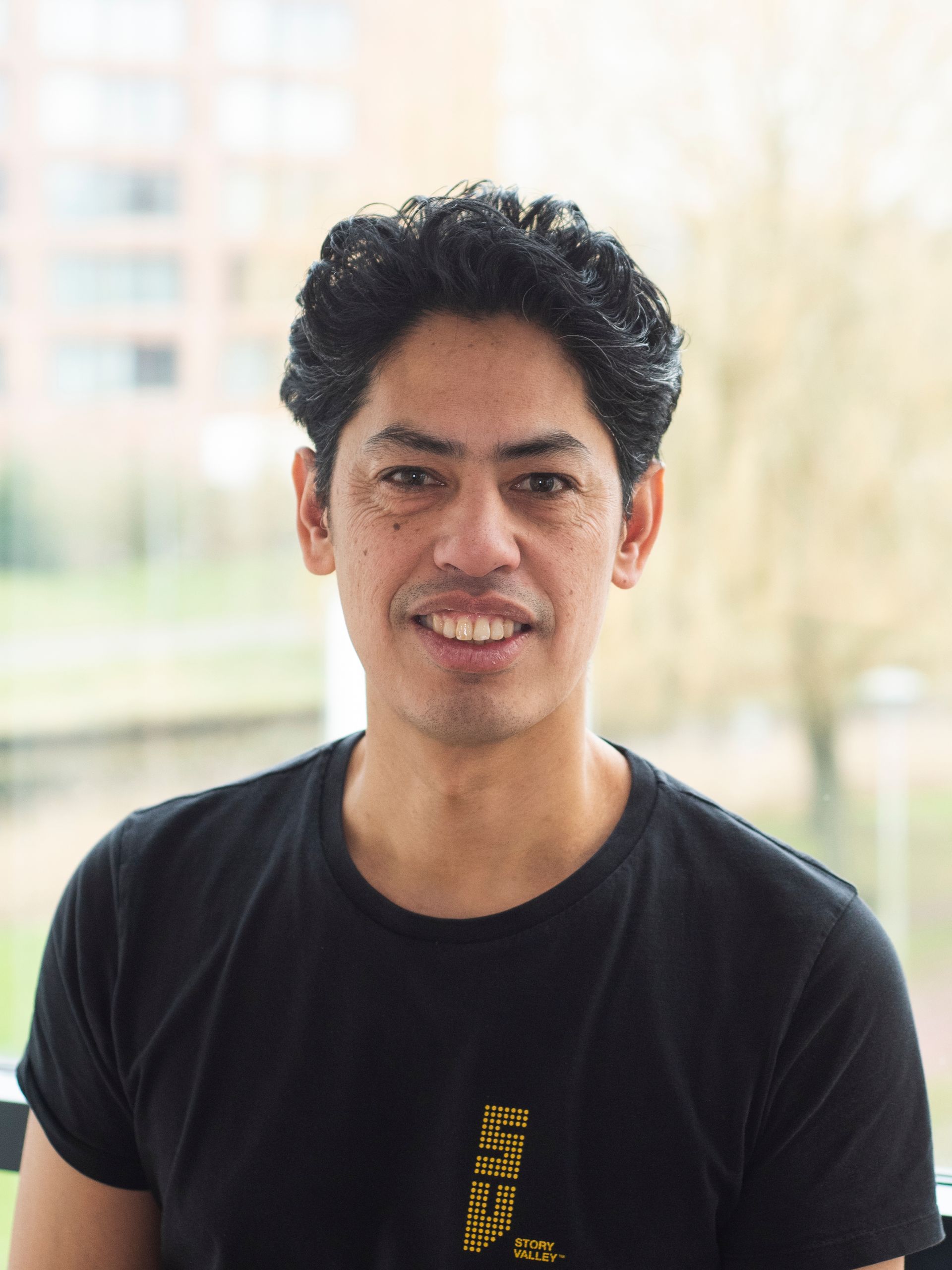 Een man in een zwart t-shirt lacht naar de camera.