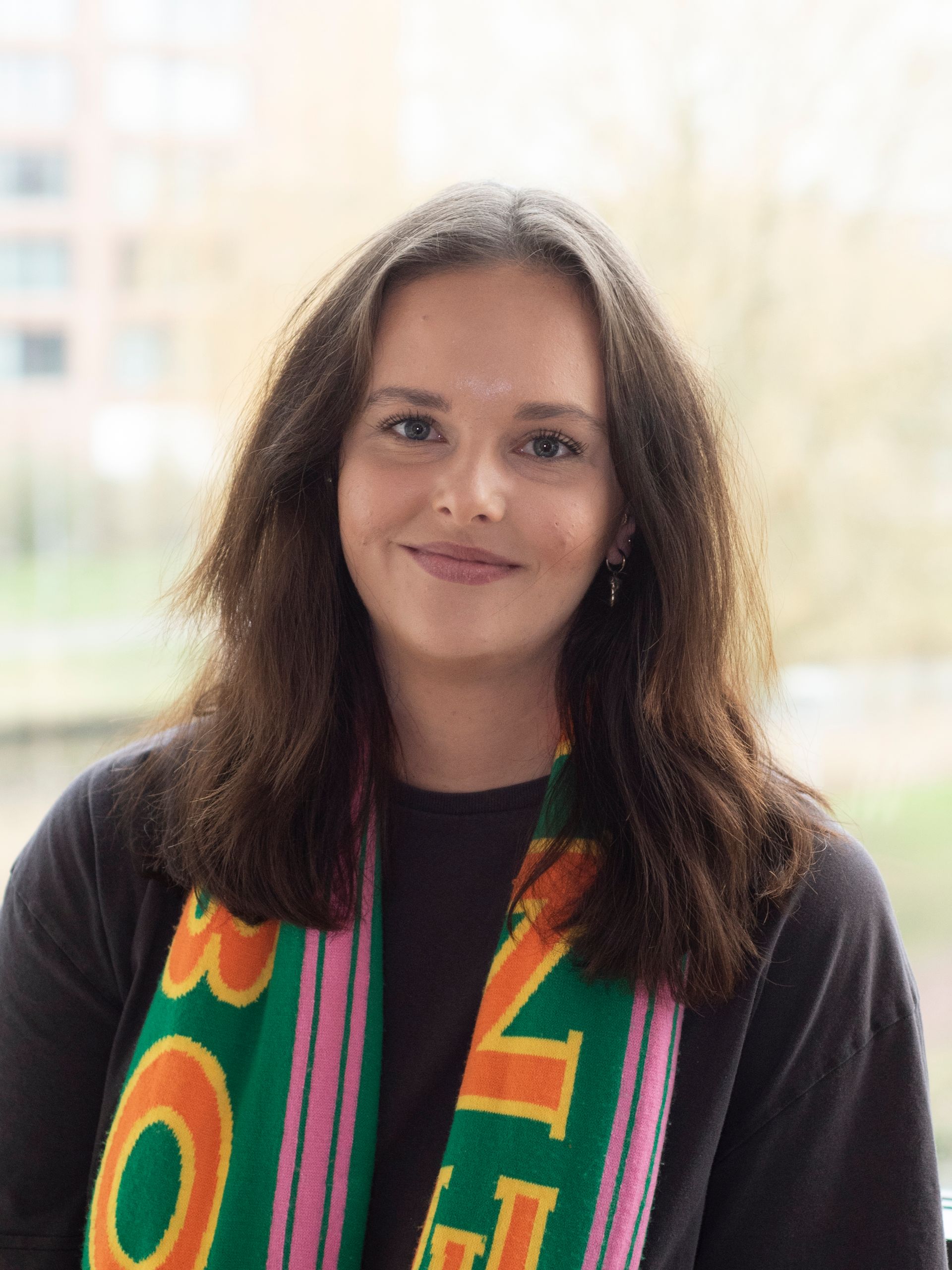 Een vrouw draagt ​​een groen en roze sjaal en lacht naar de camera.