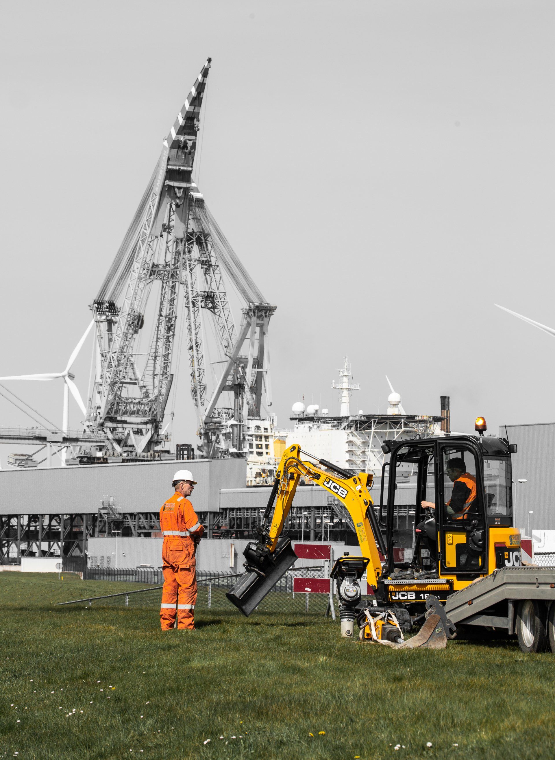 Een man die naast een gele graafmachine in een veld staat