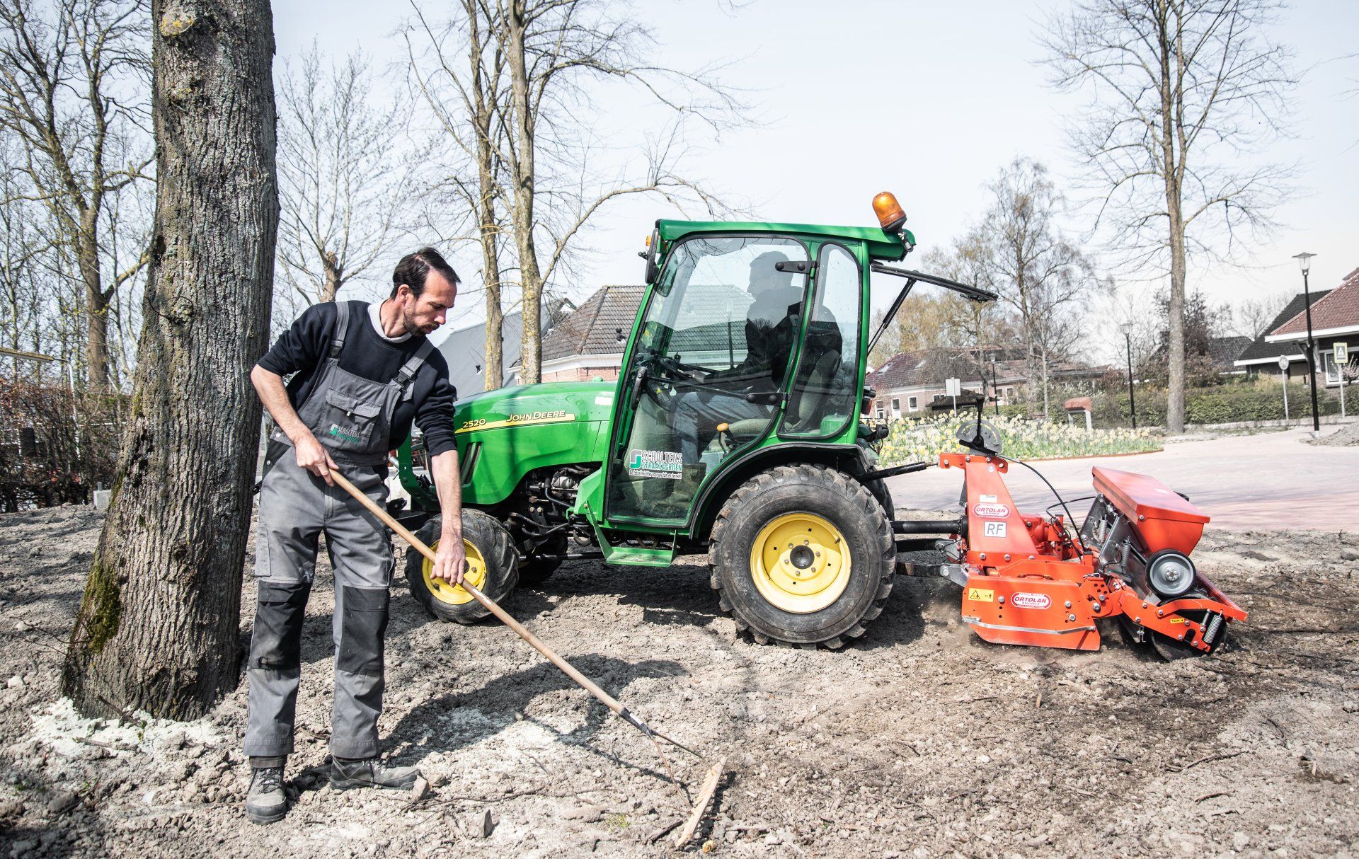 Een man harkt aarde voor een groene tractor.