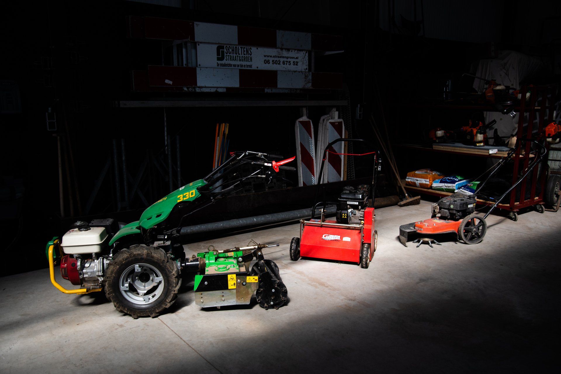Een groene tractor staat geparkeerd naast een rode grasmaaier in een donkere kamer.