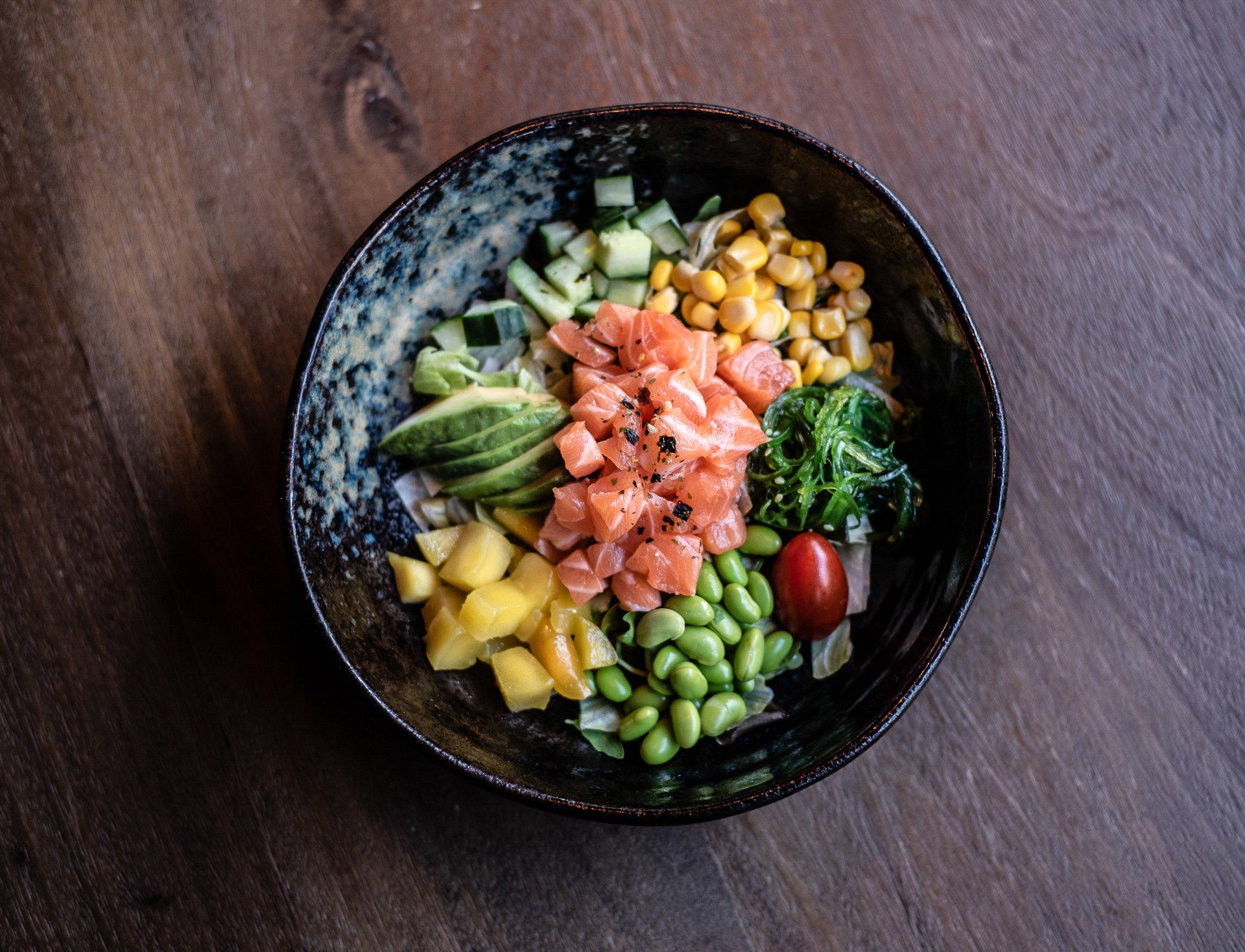 Een kom met eten, groenten en zalm op een houten tafel.