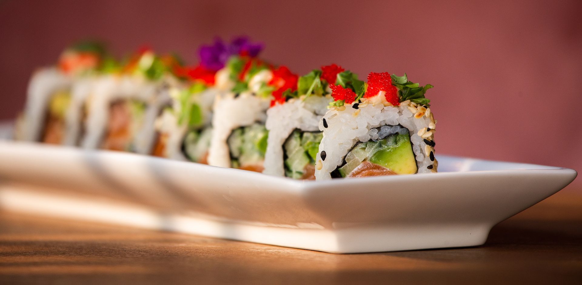 Een wit bord met sushirollen op een houten tafel.