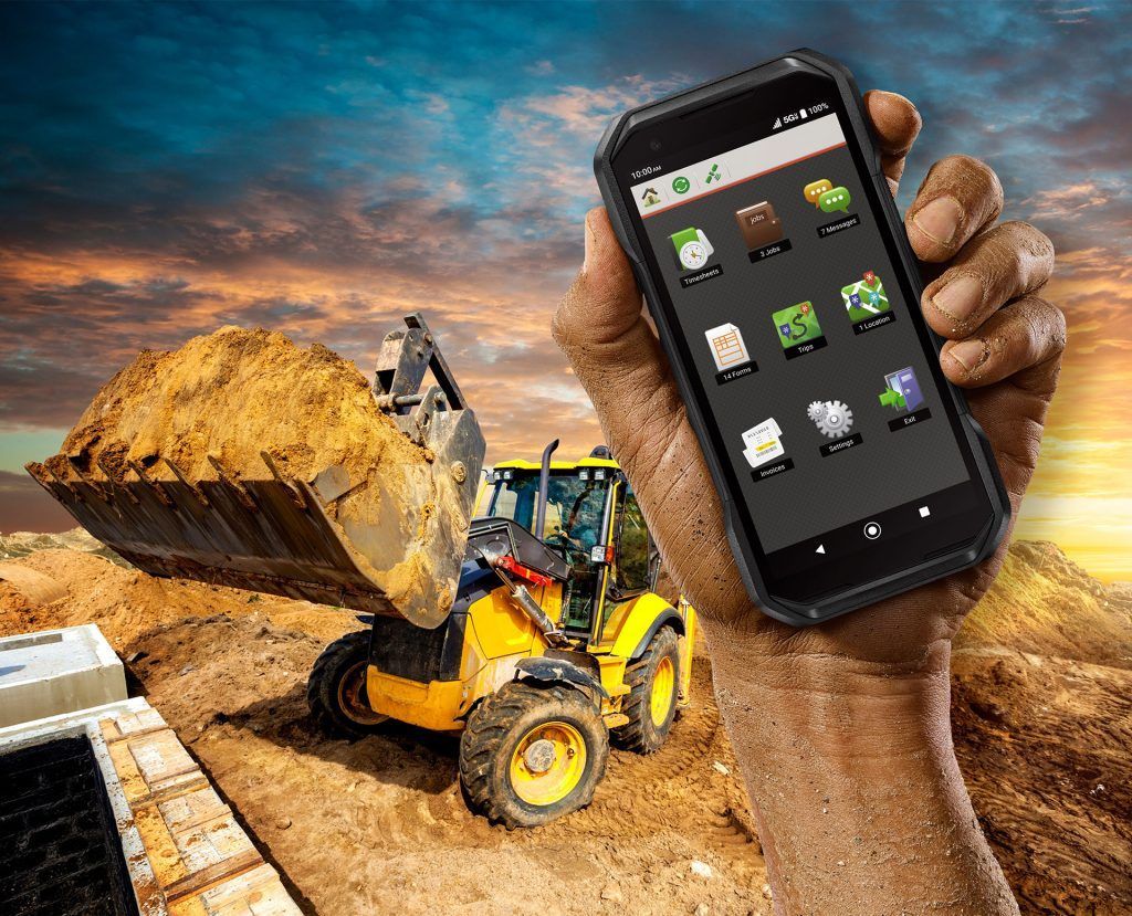 A person is holding a cell phone in front of a bulldozer.