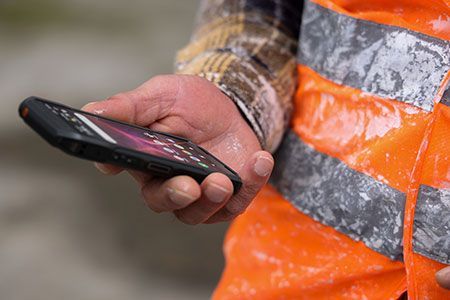 A man in an orange vest is holding a cell phone in his hand.