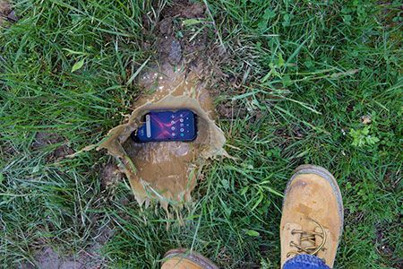 A person is standing next to a cell phone that has fallen into the grass.
