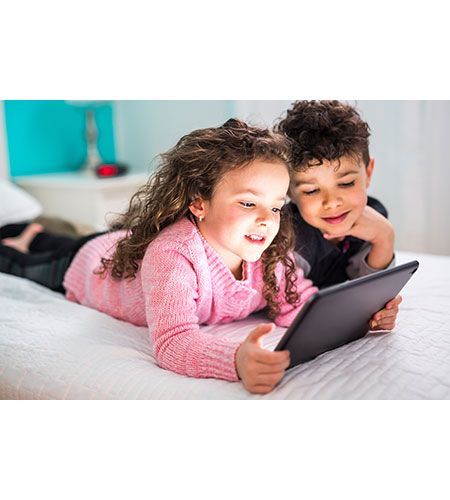 A boy and a girl are laying on a bed looking at a tablet.