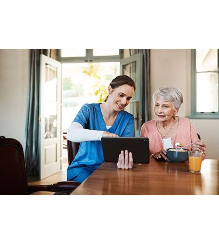 A nurse is teaching an elderly woman how to use a tablet computer.