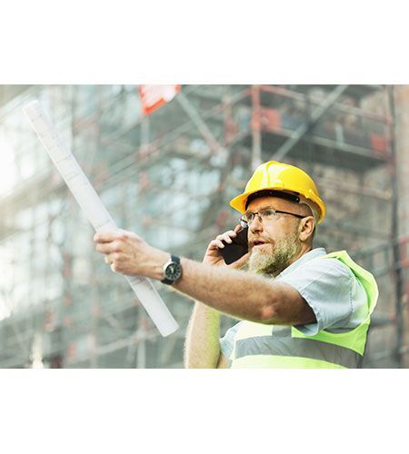 A construction worker is talking on a cell phone while holding a blueprint.