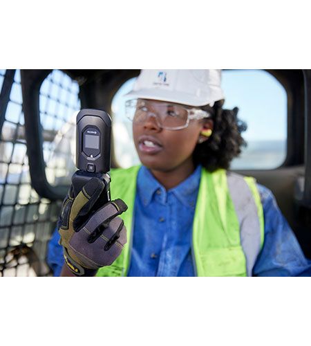 A woman wearing a hard hat and safety vest is holding a cell phone.