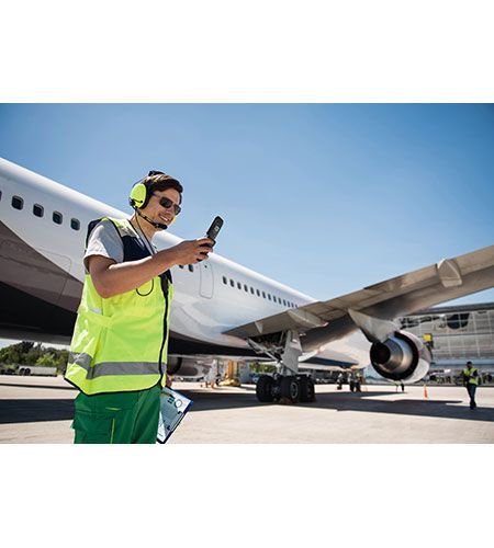 A man is standing in front of an airplane holding a cell phone.