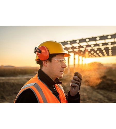 A construction worker is talking on a walkie talkie at a construction site.