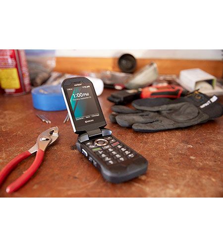 A flip phone is sitting on a table next to a pair of pliers and gloves.