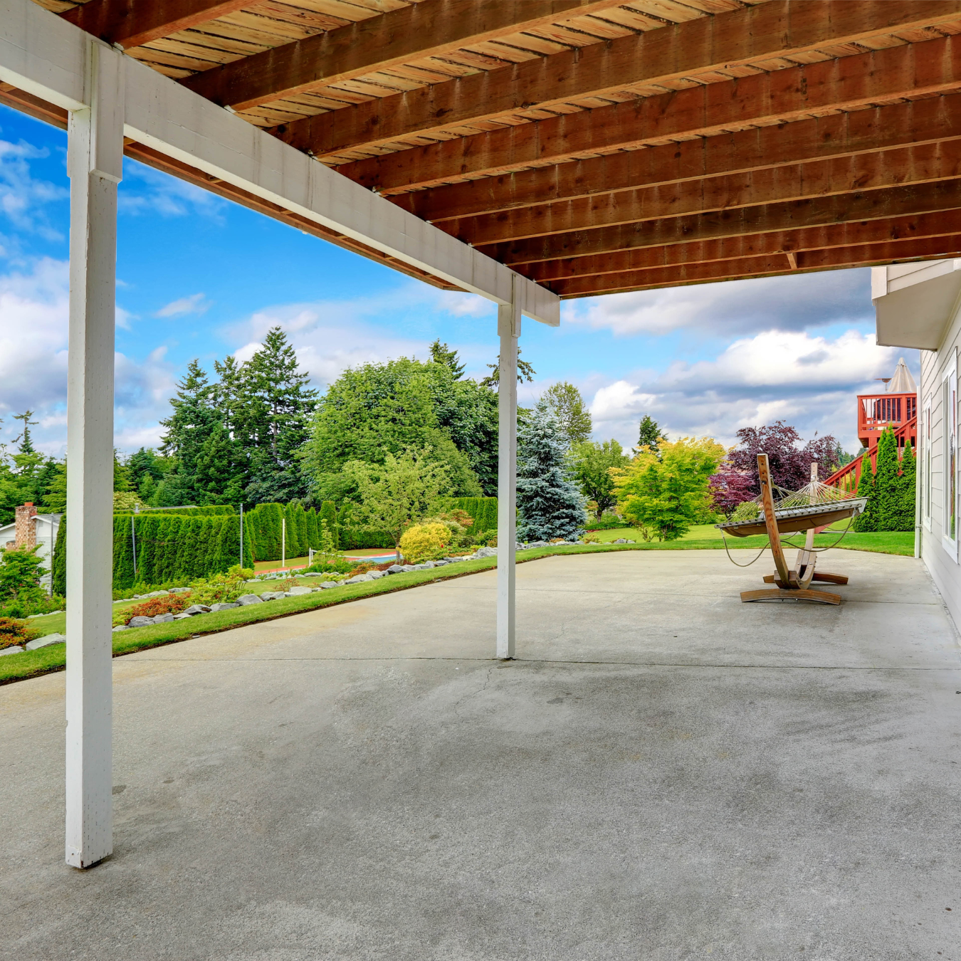 An empty patio with a wooden roof and a bench