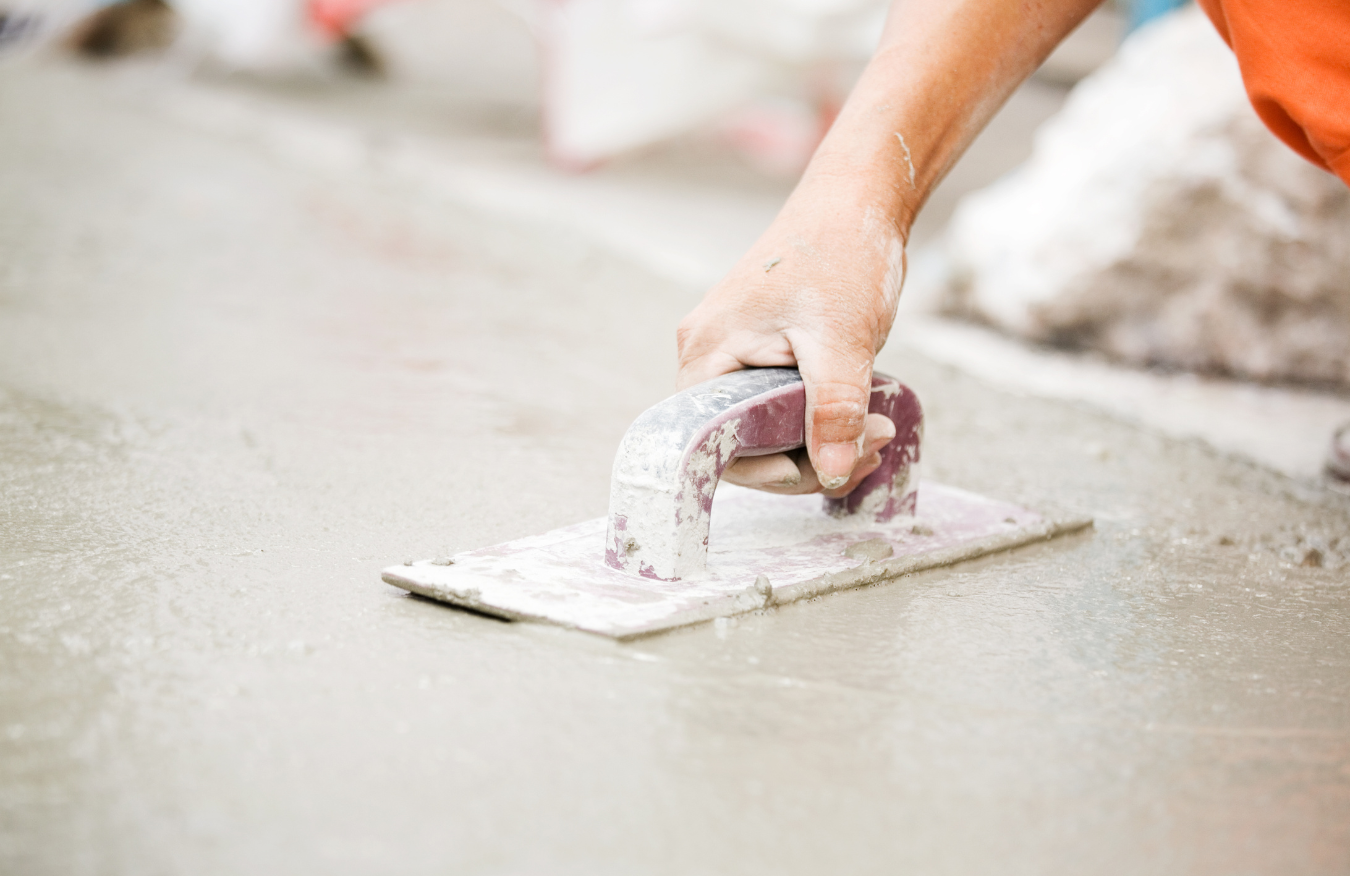 A person is plastering a concrete floor with a trowel.