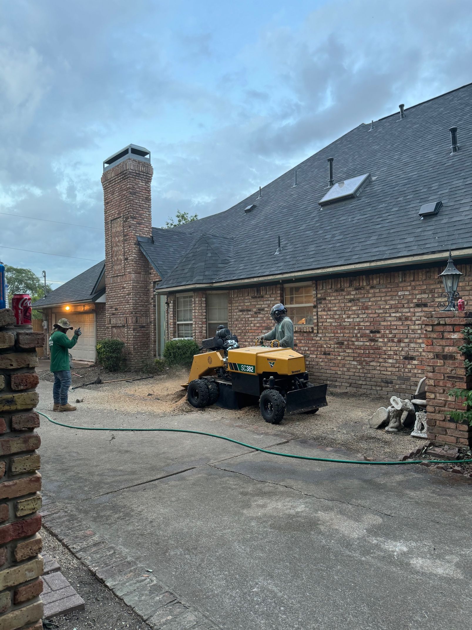 A tree stump grinder is being used to remove a tree stump in front of a house.