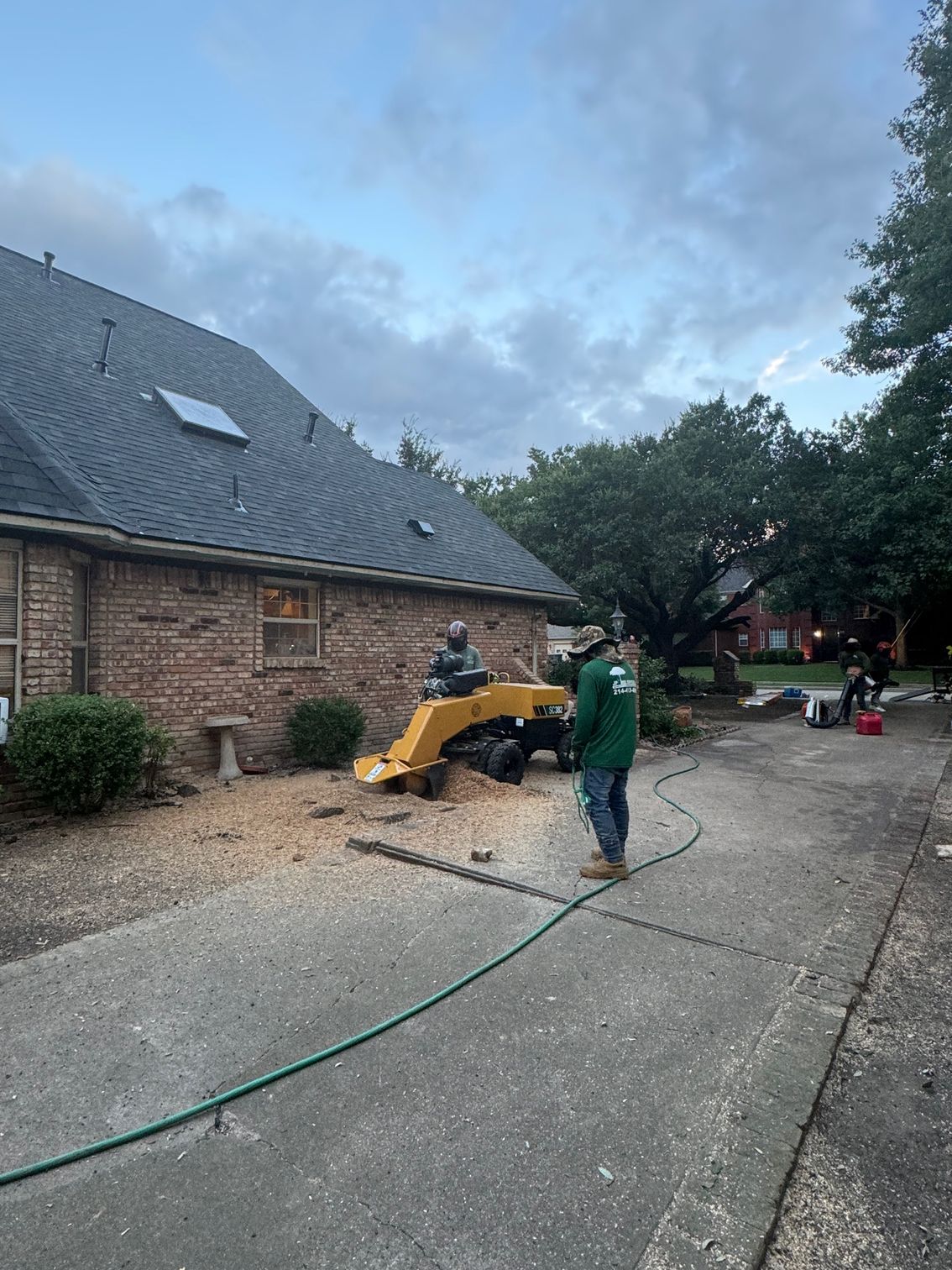 A man is standing next to a tree stump grinder in front of a house.