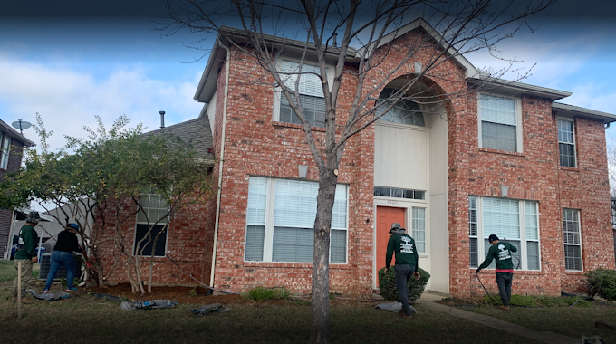 A group of people are standing in front of a large brick house.
