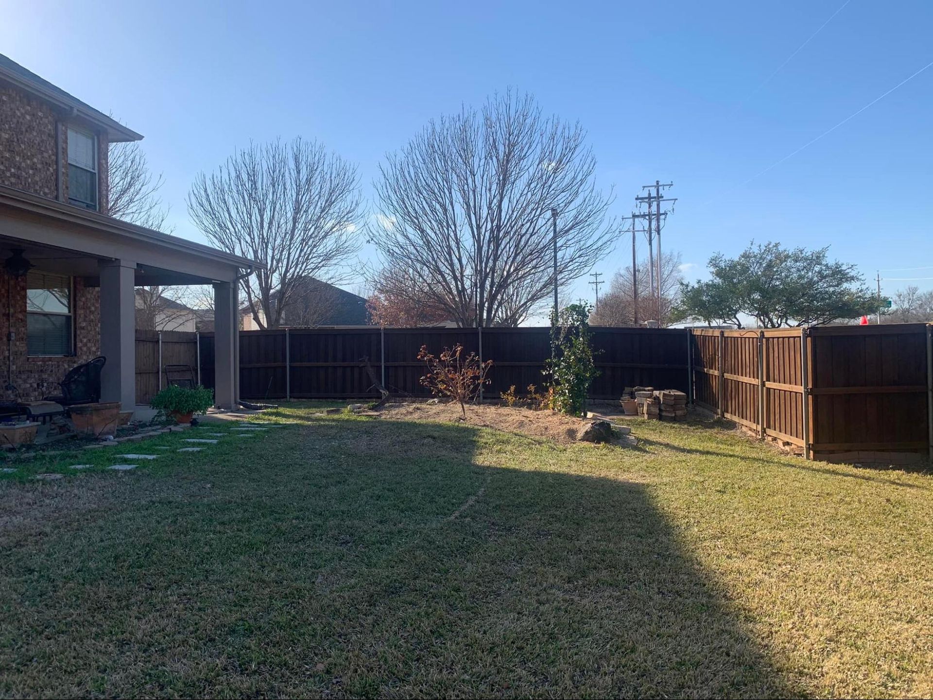 A backyard with a wooden fence and a house in the background.