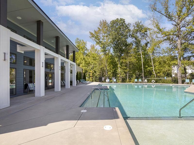 Outdoor pool at a multifamily community with a spacious deck and surrounding trees.